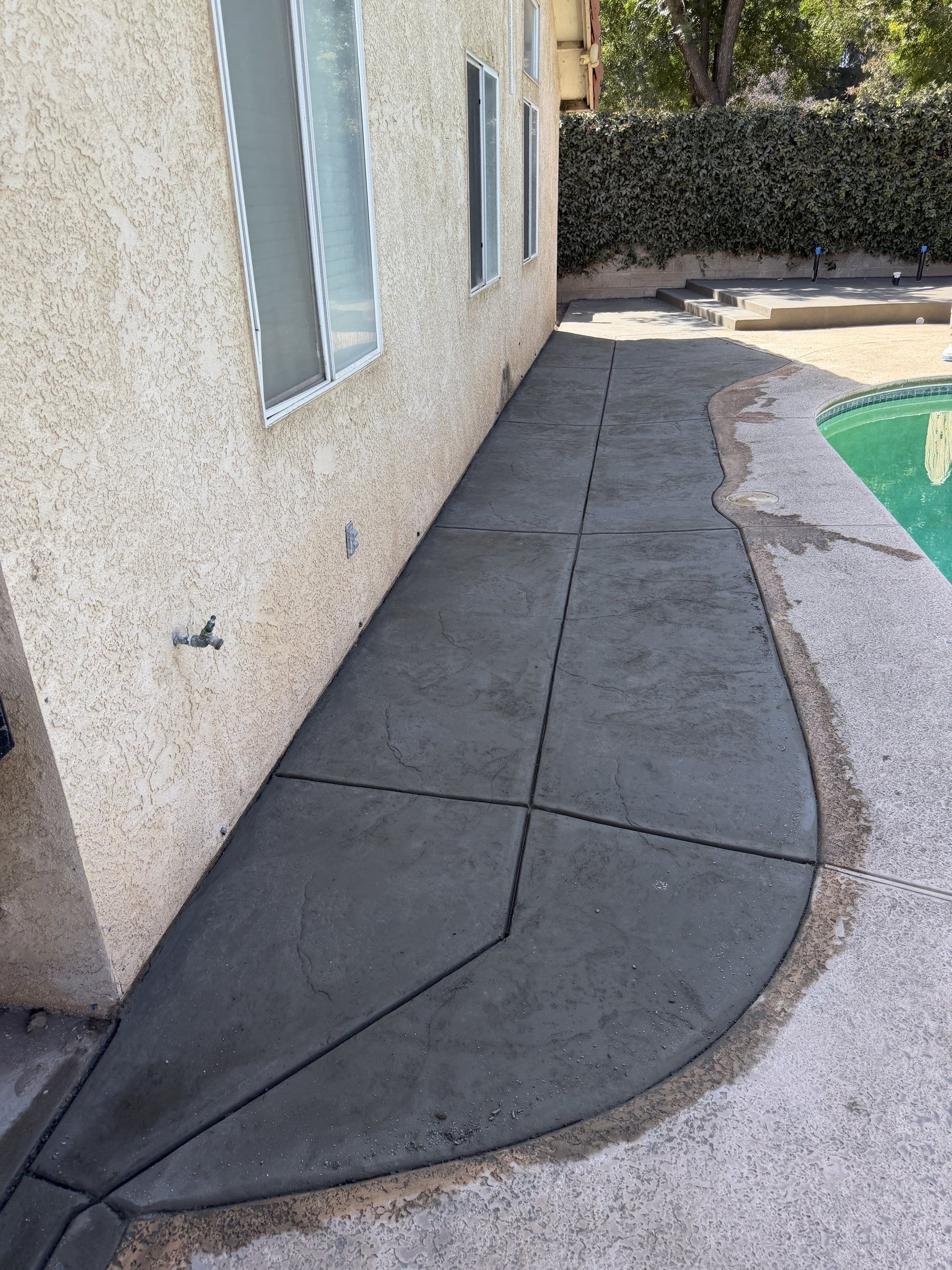 Curved concrete walkway along the side of a house next to a pool