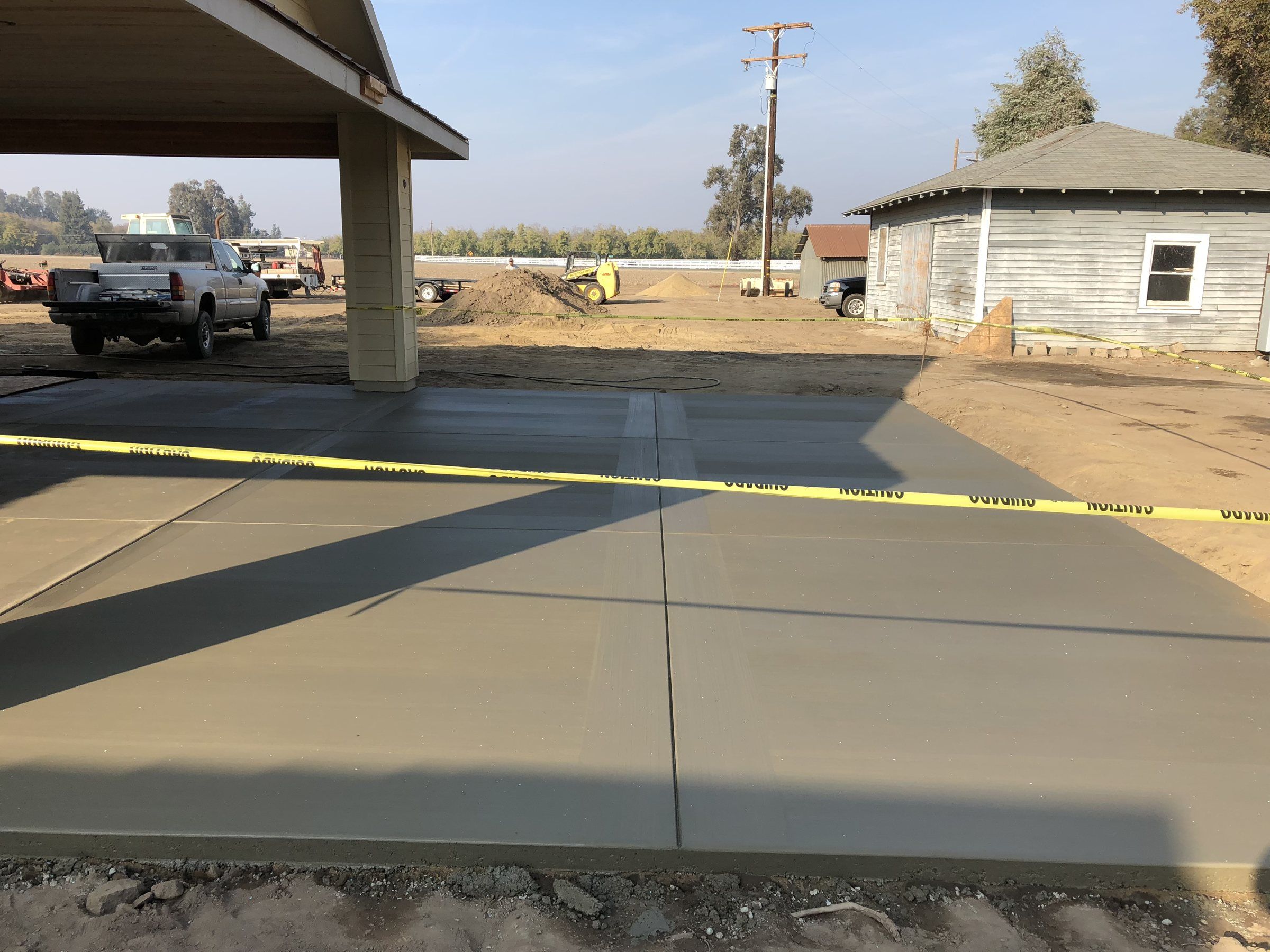 Concrete pad poured under a carport with a work truck beyond it