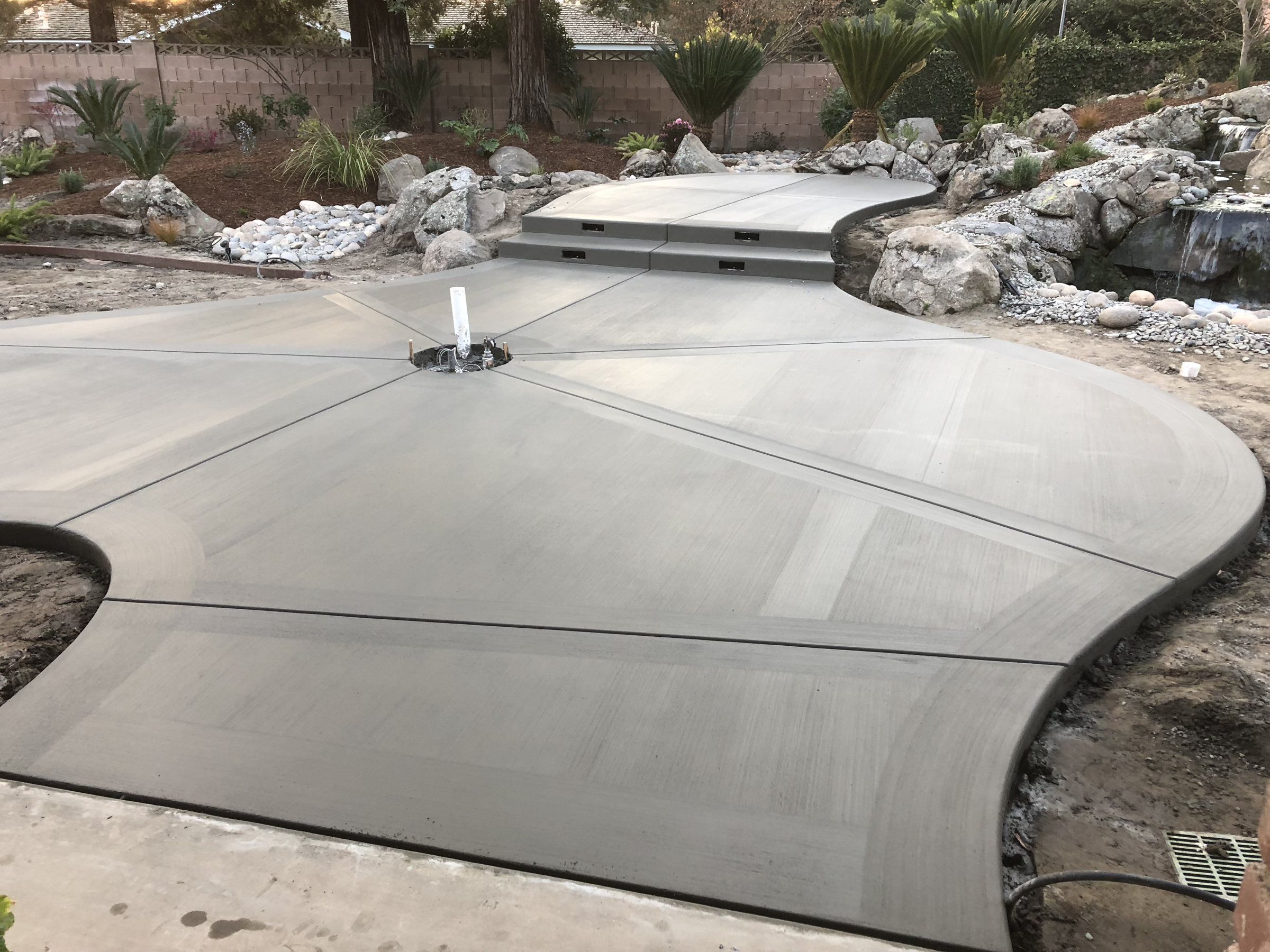 Freeform concrete patio with radial joints and a raised step, set into rock landscaping