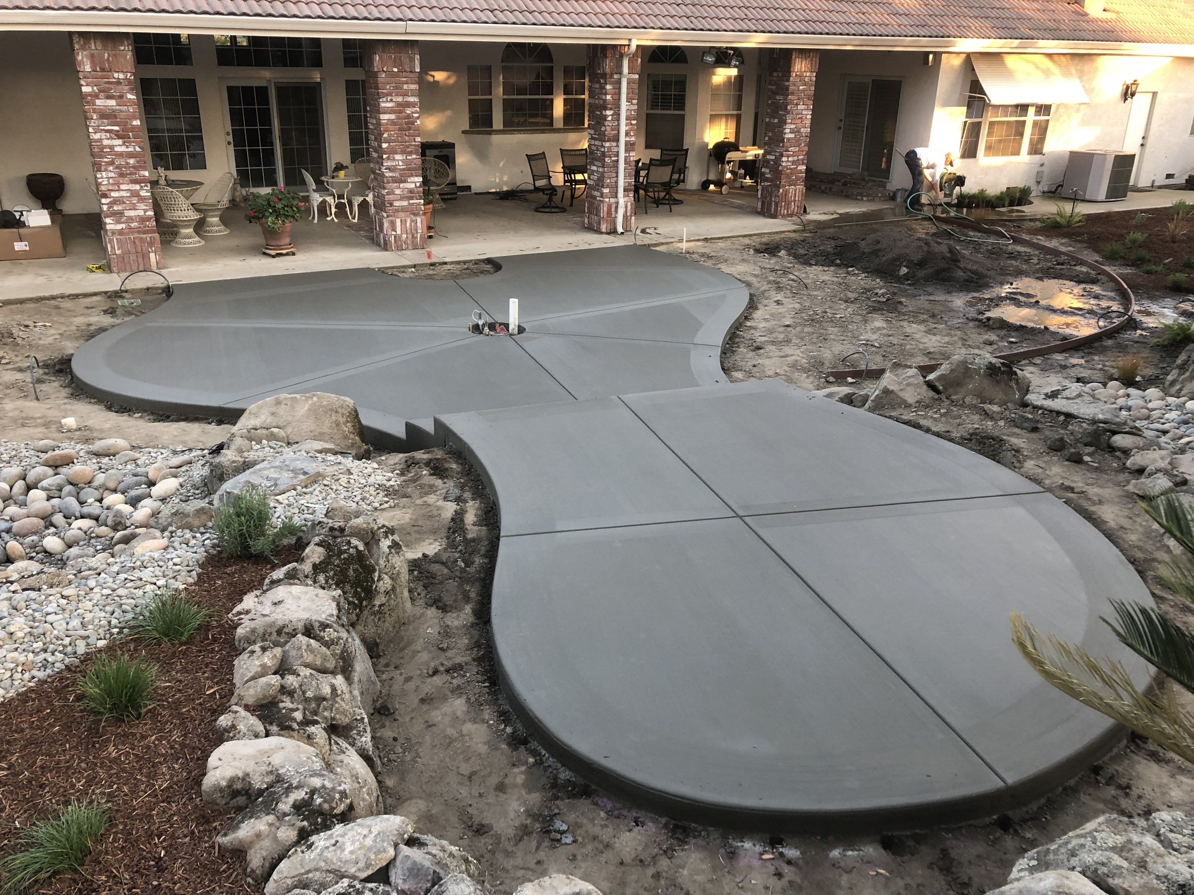 Curved freeform concrete patio wrapped by river rock landscaping