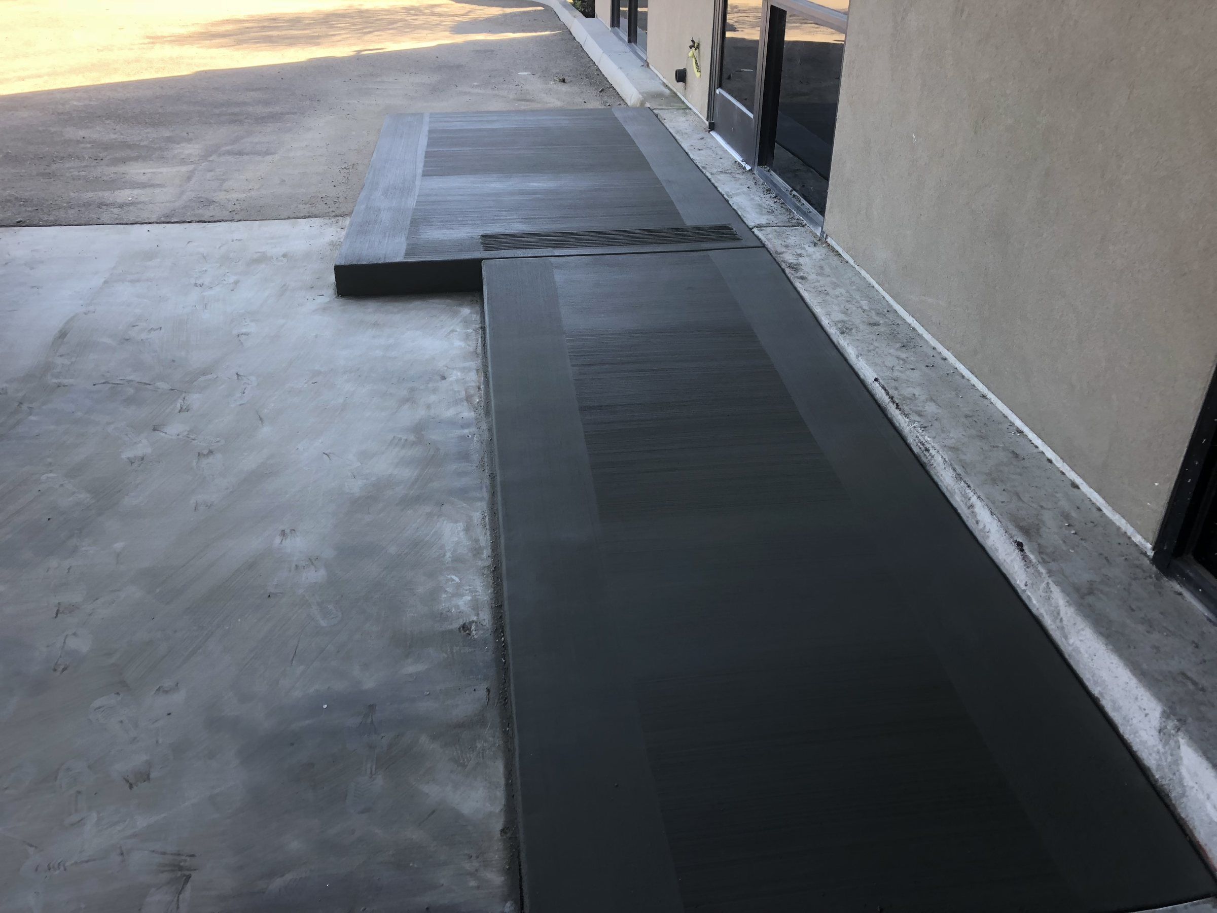 Dark-toned concrete walkway with a smooth border along a house